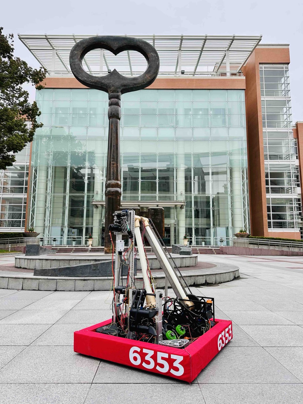 Competition robot with a telescoping arm, on pavement outside a glass building