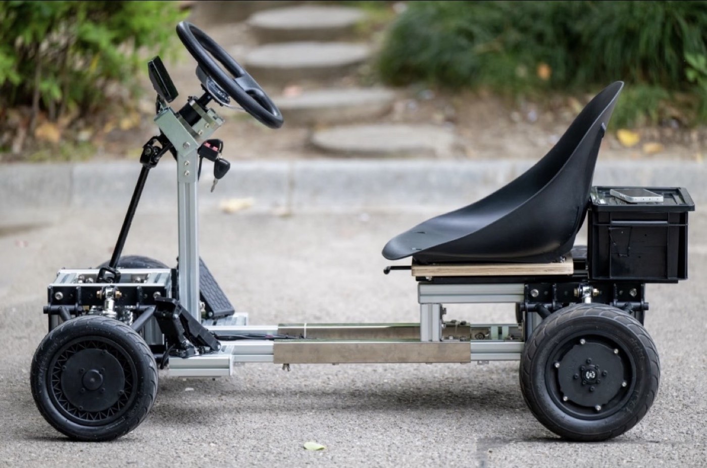 Side view of a tubular-frame go kart with a black seat, steering column and four road wheels