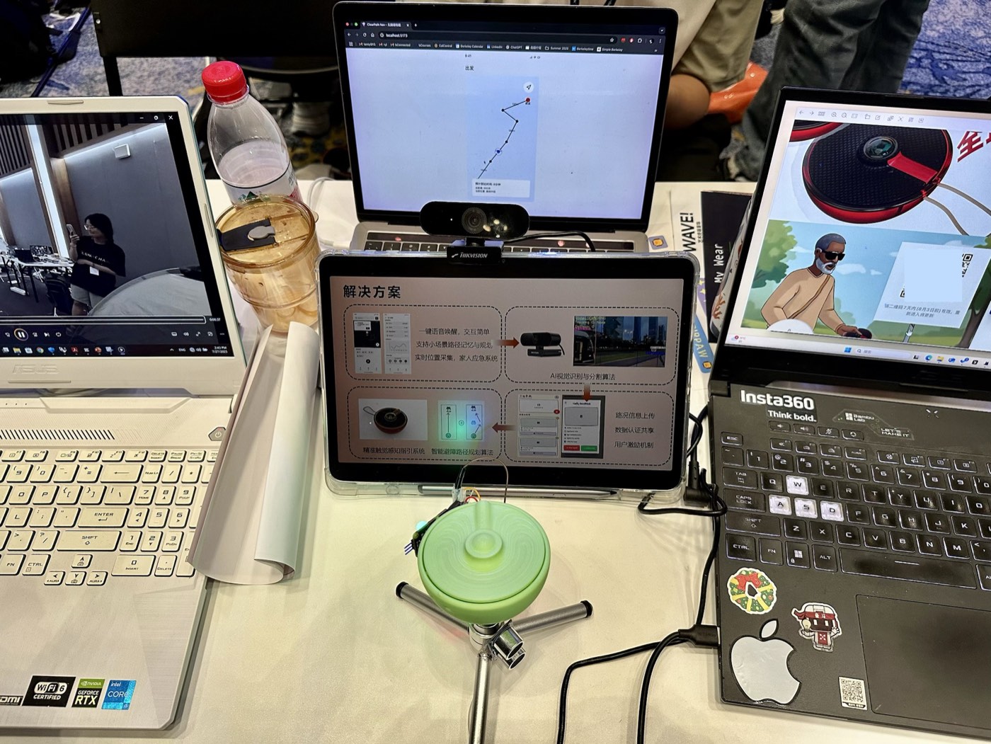 Green disc-shaped haptic device on a stand, in front of laptops showing the project's slides
